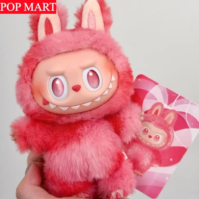 A pink fluffy Labubu collectible plush doll with large eyes and white teeth is held in a hand.