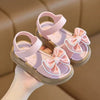 Pair of pink girls summer sandals with bow details shown being held by a hand.