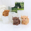 Three silicone molds of Highland cows in brown and tan colors displayed next to candles and a framed print.