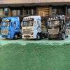 Three diecast model trucks of different colors, including blue, white, and black, parked on a green surface.