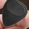 A hand holds a black guitar pick with an anti-slip grip texture.