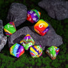 A set of colorful silicone polyhedral dice resting on green grass among dark rocks.