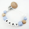 A personalized pacifier clip featuring wooden beads and silicone teeth in white and light blue colors.