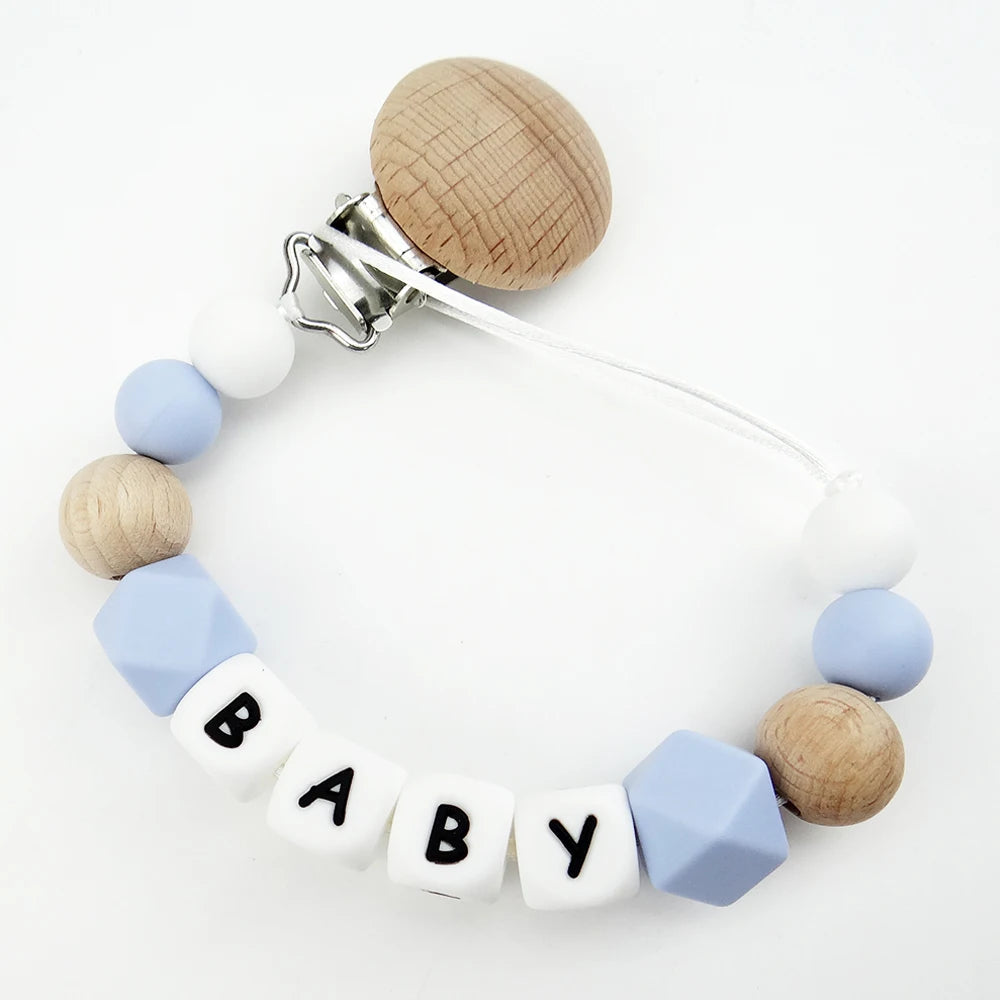 A personalized pacifier clip featuring wooden beads and silicone teeth in white and light blue colors.