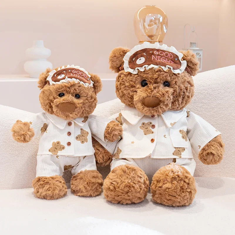 A fluffy brown teddy bear plush toy wearing a white shirt and an eye mask with the words good night