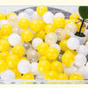 A collection of yellow and white plastic play balls are displayed in a black basket.