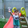 A young boy is playing with a bright orange slide and a yellow climbing structure outdoors.