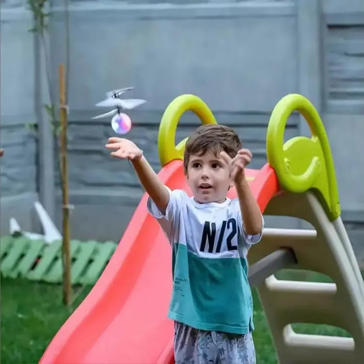 A young boy is playing with a bright orange slide and a yellow climbing structure outdoors.