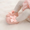 Pinke Blumensandalen auf einem Babyfuß, kombiniert mit weißen Strickstrümpchen.