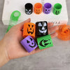 A hand holds various colored Halloween pumpkin coil spring toys for party favors.