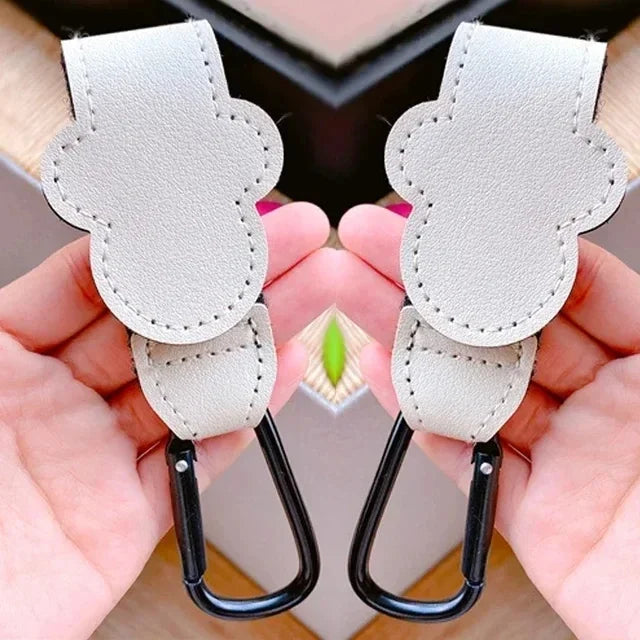 A pair of light gray PU leather stroller organizer hooks being held in a person's hand.
