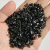 A hand holds a pile of dark, natural tumbled stone chips for jewelry making and home decor.