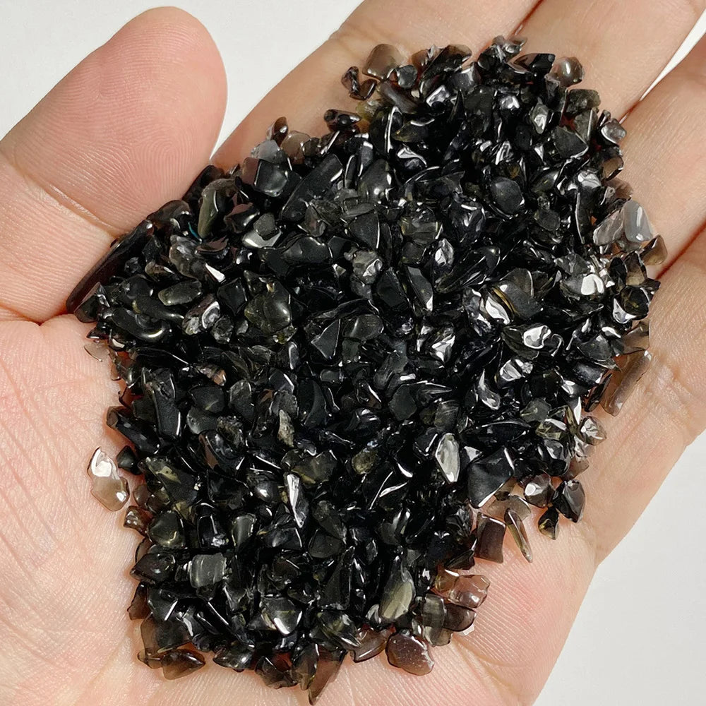A hand holds a pile of dark, natural tumbled stone chips for jewelry making and home decor.