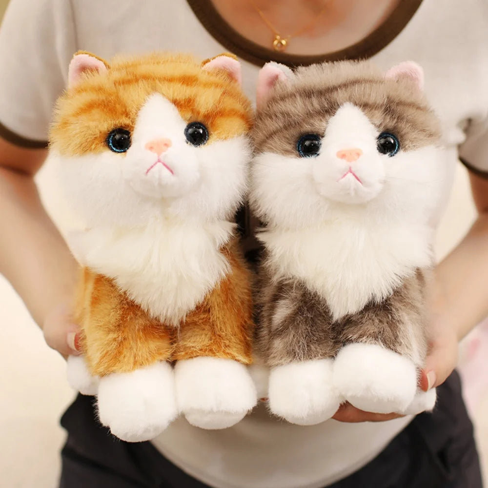 A pair of fluffy orange and gray kitten plush toys being held by a person.