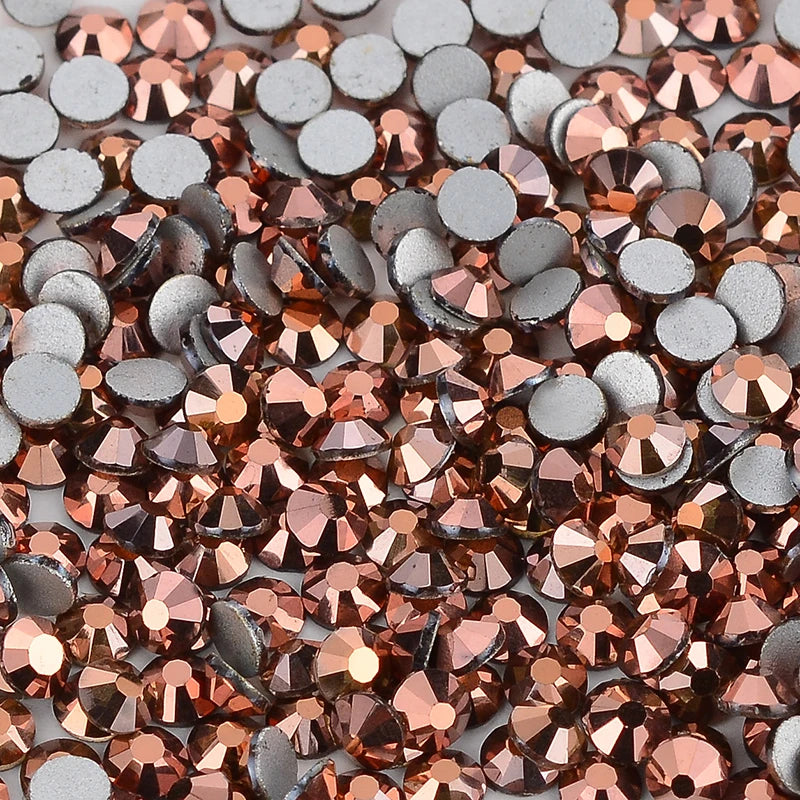 A close-up view of various flatback rhinestones in silver and rose gold tones for nail art and crafts.