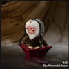 A plush doll resembling a creature with white fur and black stripes sits on a red tray against a dark background.