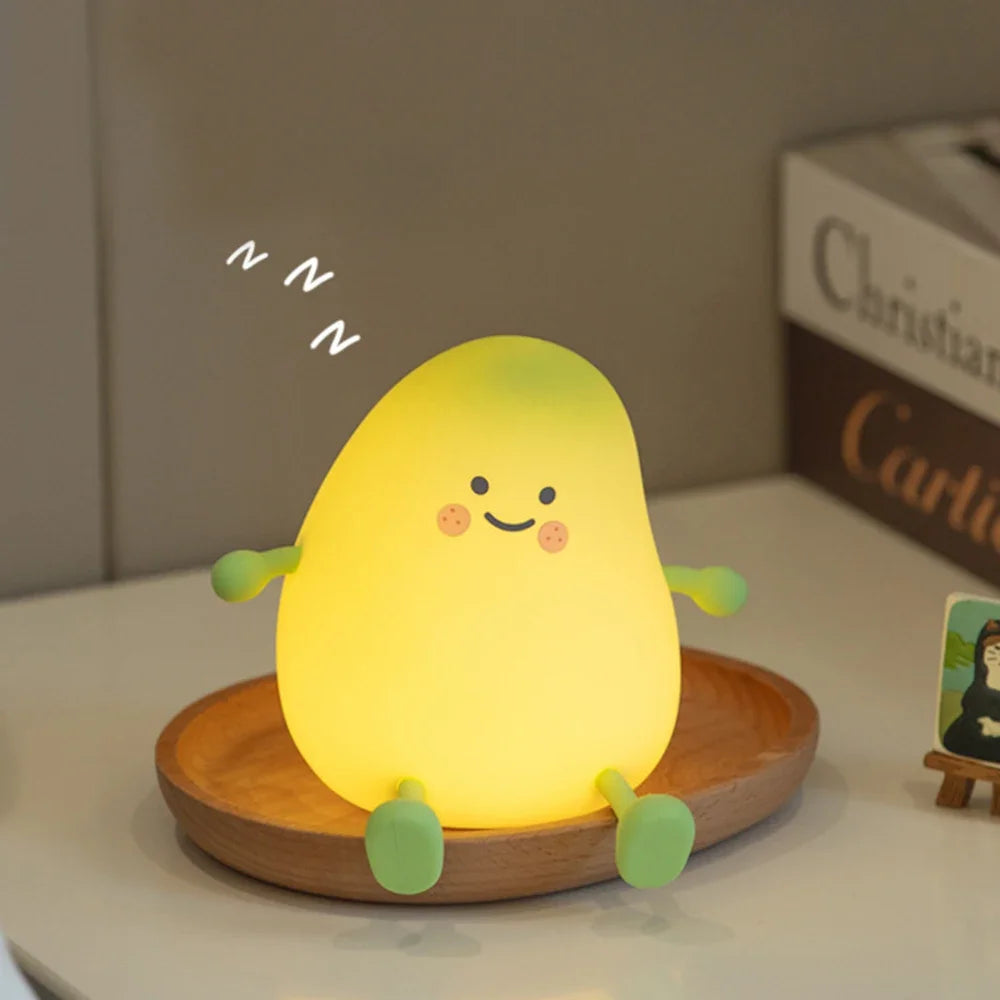 A glowing yellow pear-shaped night light with smiling face and green accents sitting on a wooden coaster.