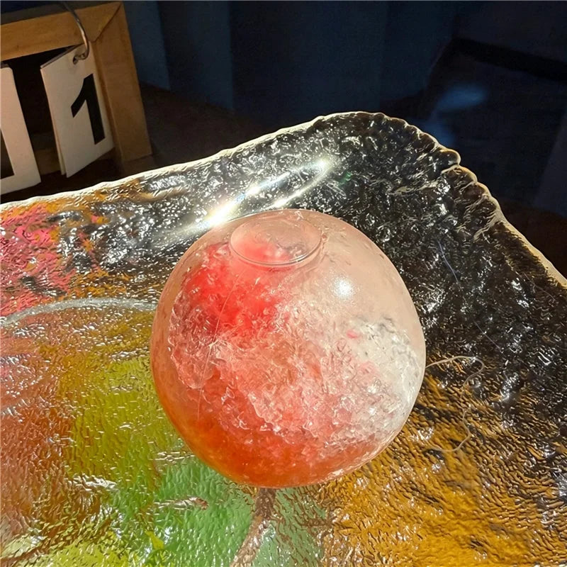 A translucent, spherical fruit squishy stress relief ball with pink and red hues resting on a reflective surface.