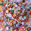 A colorful assortment of miniature dollhouse snack foods including candies, cookies, and savory items.