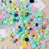 A colorful mix of iridescent resin and rhinestone pearls in various shades of pink, green, yellow, and blue scattered on a li