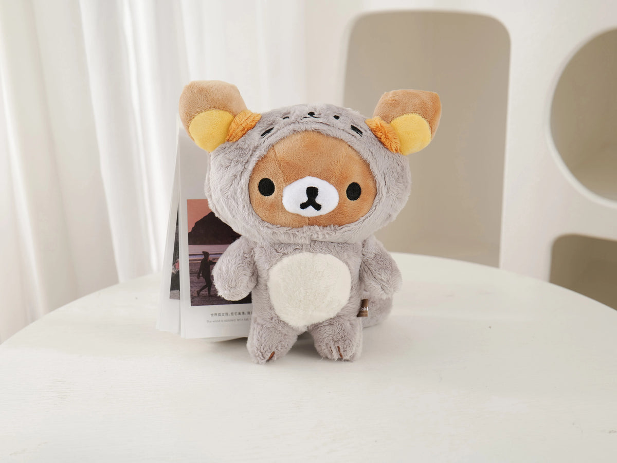 A soft gray Rilakkuma anime plush bear with orange ears and a white chest sitting on a white surface.