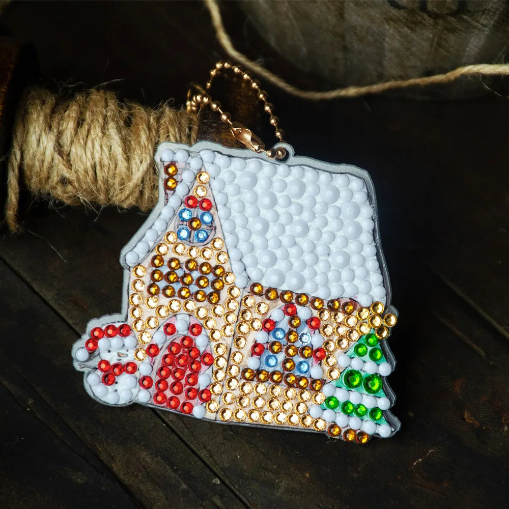 A white diamond painting charm pendant featuring colorful rhinestones and a house design, attached to a gold-colored keychain