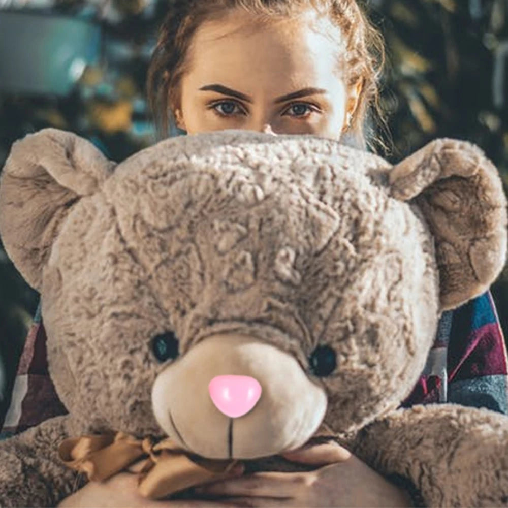 A young girl is holding a fluffy brown teddy bear with a pink nose and safety eyes.