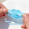 A hand is squeezing a blue, translucent silicone squishy toy shaped like a cat paw on a white surface.