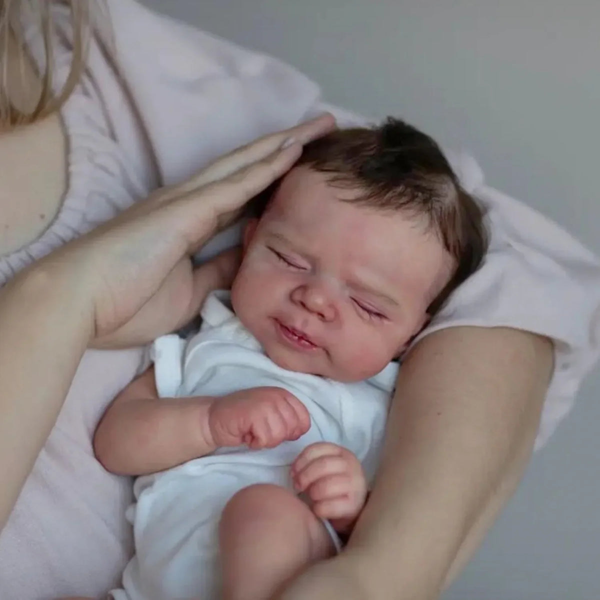 A newborn baby with hand-rooted hair is being held by an adult's hand.