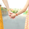 Two hands are clasped together, showing jewelry with yellow and orange glass beads.