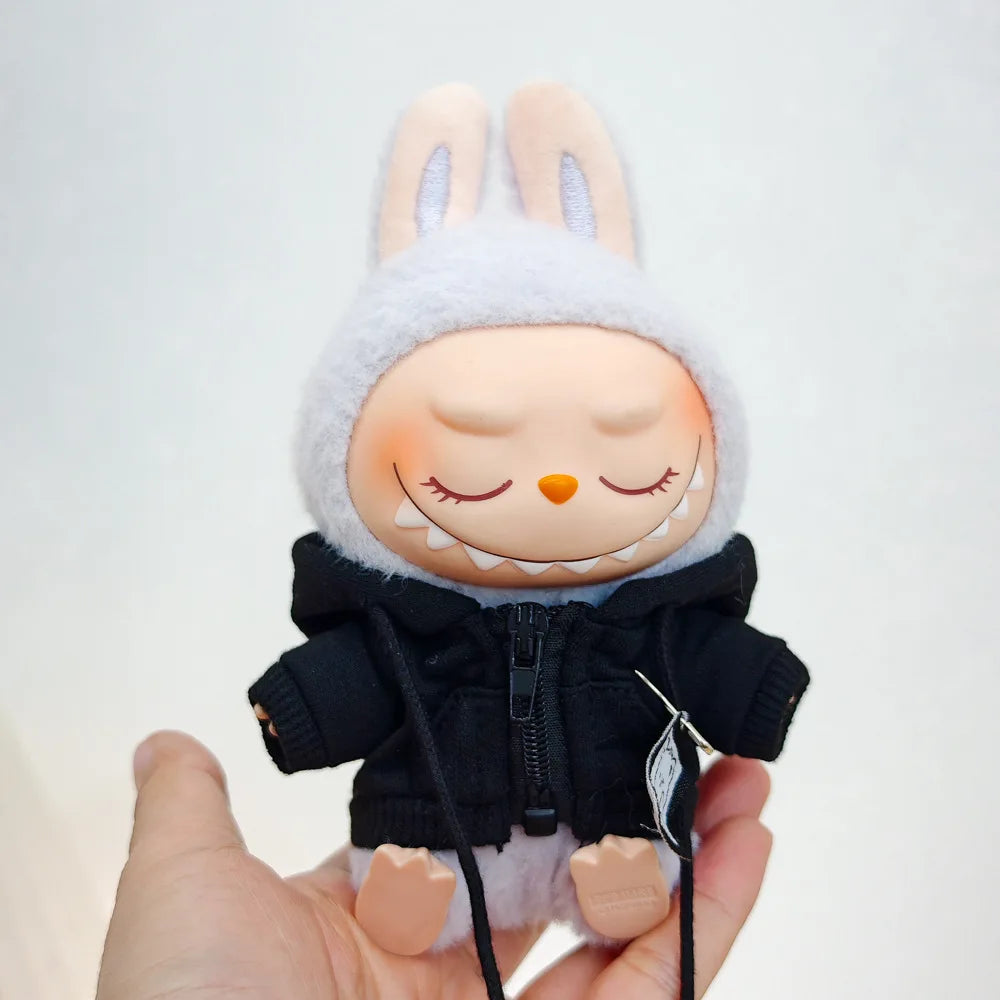 A Labubu doll wearing a black bear hoodie with headphones, held in a person's hand.