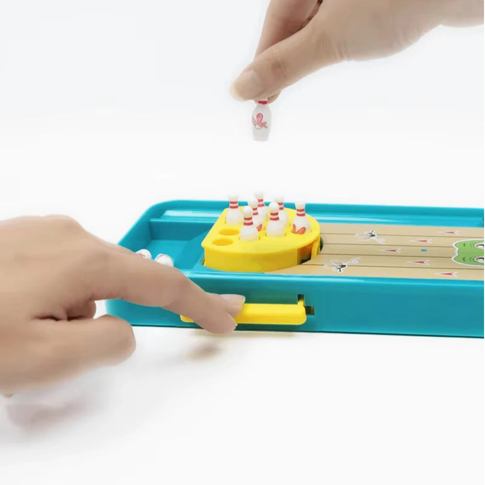 A hand is placing a small white frog onto a yellow bowling pin in a blue plastic game set.