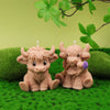A set of four silicone candle molds shaped like adorable Highland cows sitting on green grass with a leafy branch overhead.