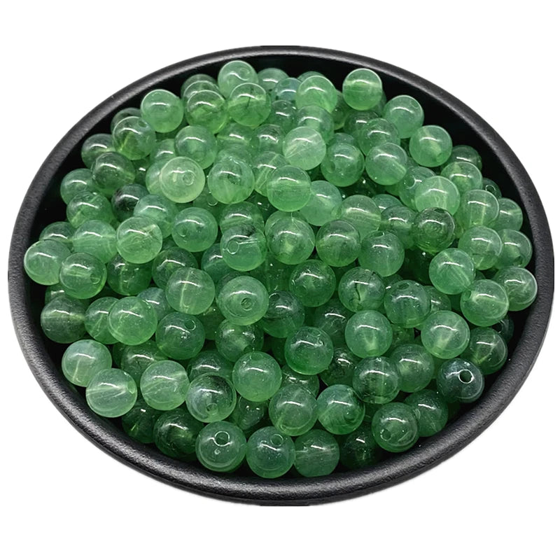 A pile of translucent green acrylic round beads for jewelry making in a black bowl.