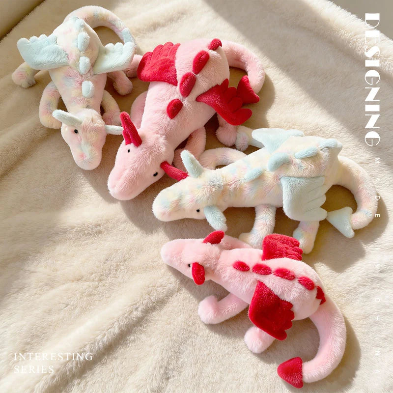 A collection of pink and red dragon plush toys resting on a light beige fuzzy surface.
