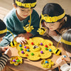 Children playing with a yellow bumblebee board game and fishing toy set on a wooden table.