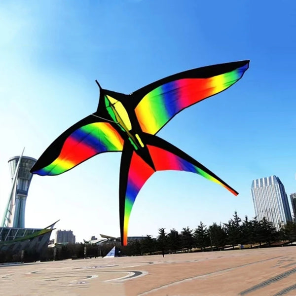 A vibrant rainbow nylon kite is shown flying against a clear blue sky.