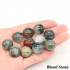 A collection of polished Blood Stone crystal spheres in various shades of green, gray, and reddish-brown resting on a hand.