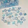 A collection of mixed acrylic bow and flower beads in various shades of blue and clear are displayed on a white surface.