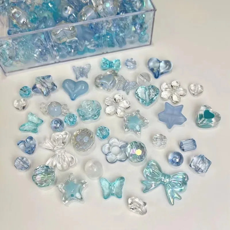 A collection of mixed acrylic bow and flower beads in various shades of blue and clear are displayed on a white surface.