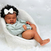 A newborn Reborn baby doll with hand-rooted hair is resting in a white fluffy nest.