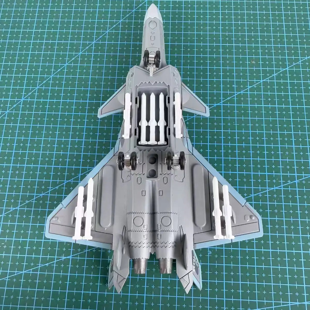 A gray military fighter jet model kit, resembling an F-14 Tomcat or similar design, is displayed on a grid surface.