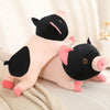 A soft, adorable plush pig stuffed animal with black and pink features lying on a light fabric.