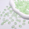 Small, translucent green glass beads are displayed in a white scoop on a white background.