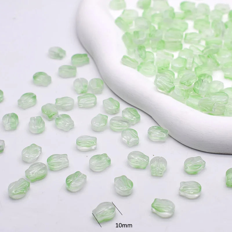 Small, translucent green glass beads are displayed in a white scoop on a white background.