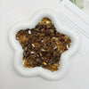 A white dish filled with gold and brown acrylic ice strips for nail art and DIY crafts.