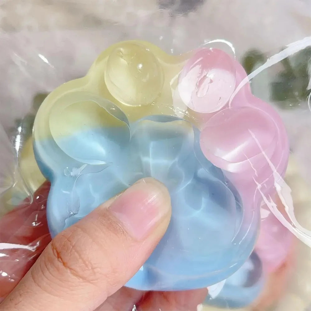 A hand holds a translucent squishy toy shaped like a cat paw in various pastel colors including yellow, blue, and pink.