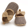 A pair of beige patterned baby walking shoes with bow details shown from above.