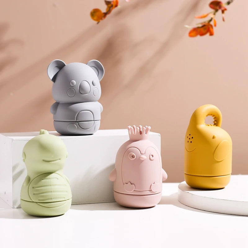 Three soft silicone animal bath toys in gray, pink, and yellow are displayed on a white surface.