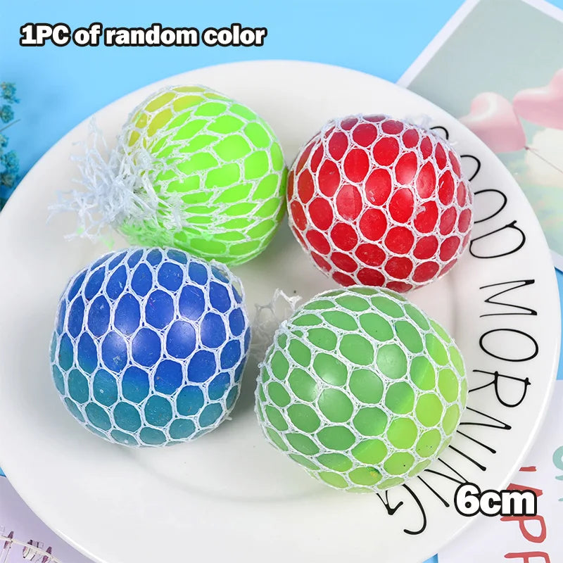 Four colorful mesh stress relief balls in green, red, blue, and lime green resting on a white plate.